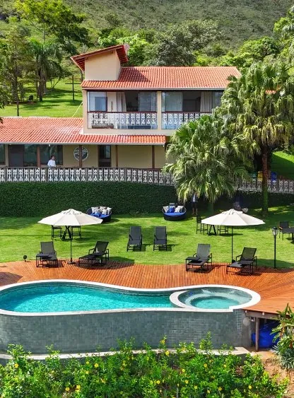 Casa principal de telhado colonial com varanda, gramado e a piscina em primeiro plano